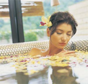 Mergaitė guli vonioje su rožių žiedlapiais
