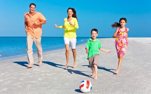 الآباء والأمهات مع الأطفال يركلون كرة على الشاطئ.
