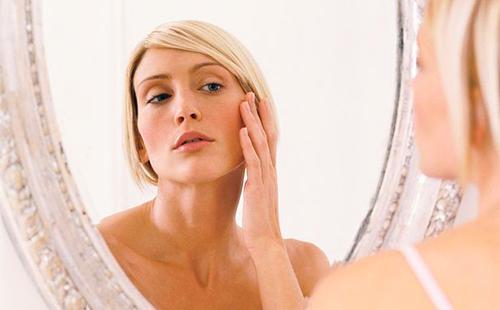 Η ξανθιά εξετάζει προσεκτικά το δέρμα στις γωνίες των ματιών σε έναν καθρέφτη