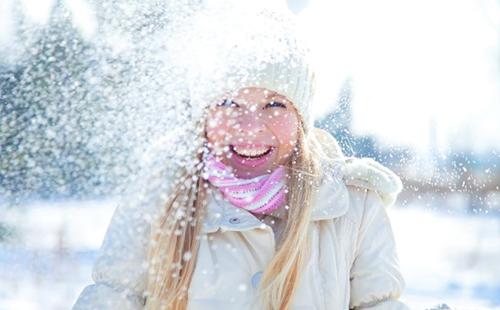Το κορίτσι σε ένα λευκό καπάκι απολαμβάνει το χιόνι