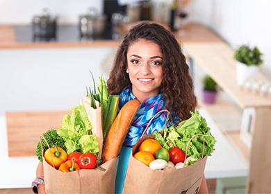 Млада жена държи в ръце пакети със зеленчуци