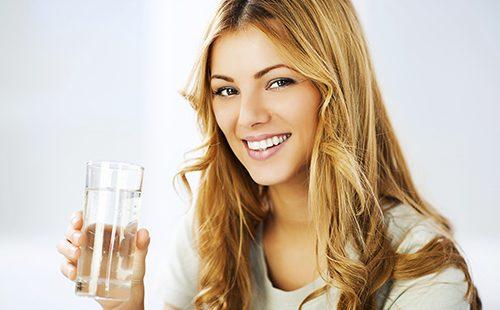 Usmívající se dívka drží sklenici vody