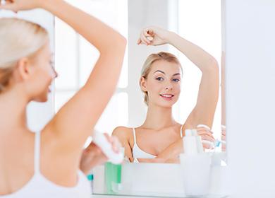 Frau mit desodorierendem Mittel vor einem Badezimmerspiegel