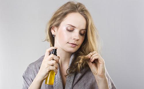 Dívka s lahví oleje zkoumá konce vlasů