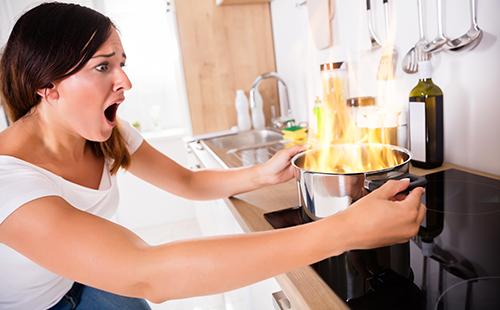 Γυναίκα με τρόμο κοιτάζει το καίγοντας φαγητό στο τηγάνι.
