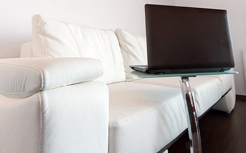 Masarap na magtrabaho sa isang laptop sa isang puting leather sofa