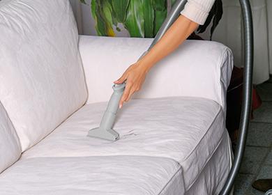 La donna pulisce un divano leggero con un aspirapolvere