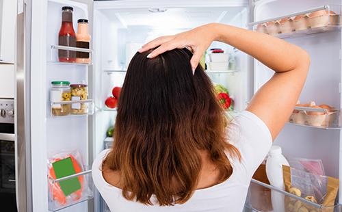 Verwirrte Frau guckt in den Kühlschrank