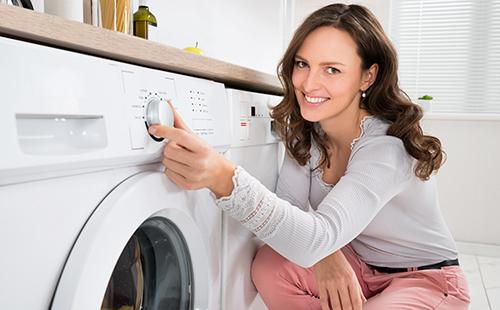 Moteris su šypsena įjungia skalbimo mašiną