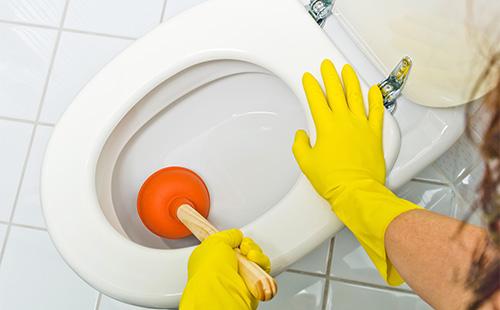 Mani in guanti gialli lavano la toilette con uno stantuffo.