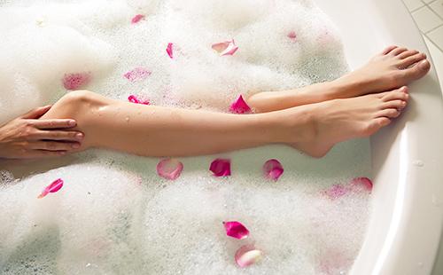Le gambe della ragazza in un bagno di schiuma con petali rosa