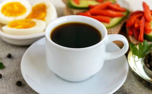Šálek silné kávy, vařená vejce a zelenina k snídani