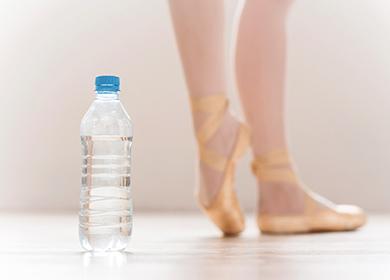 Üveg víz és balerina táncoló lábak a háttérben