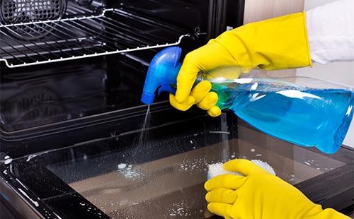 Frau wäscht den Ofen mit einem Spray