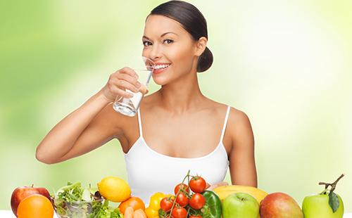Moteris baltame viršuje su stikline vandens ir vaisiais
