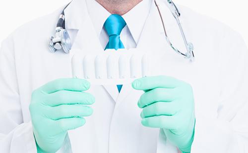 Lekárove ruky v rukaviciach držia lekárske sviečky