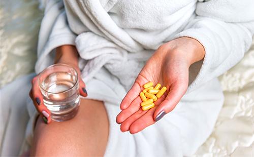 Dievča drží žlté kapsuly s liekom v ruke