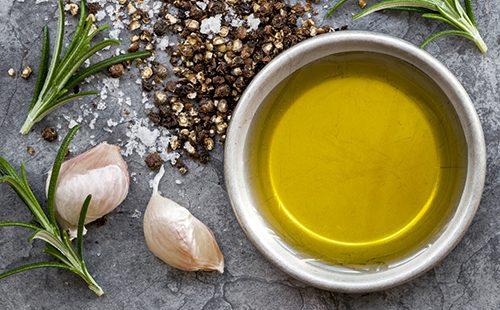 Una ciotola di olio d'oliva, due spicchi d'aglio e rosmarino