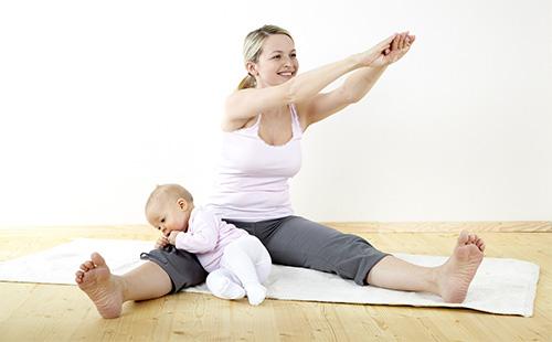 Nainen tekee harjoituksia kotona vauvan kanssa