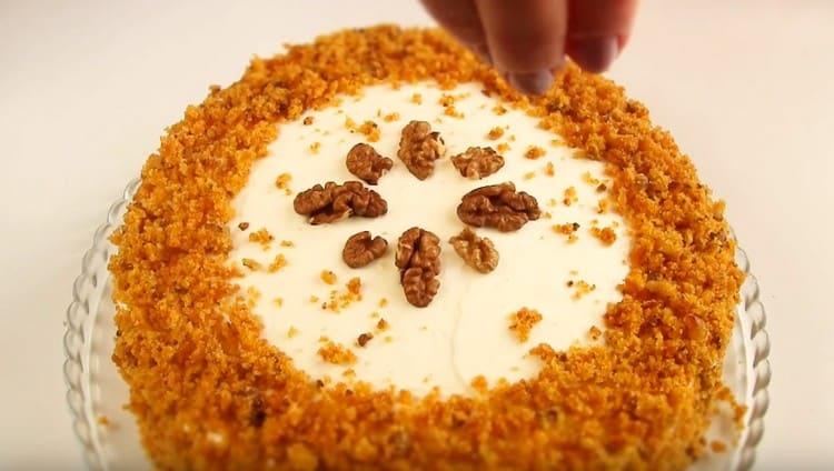 Nachdem Sie die Oberseite und die Seiten des Kuchens mit Sahne eingefettet haben, streuen Sie die Seiten mit Krümeln, verzieren Sie das Dessert mit Nüssen.