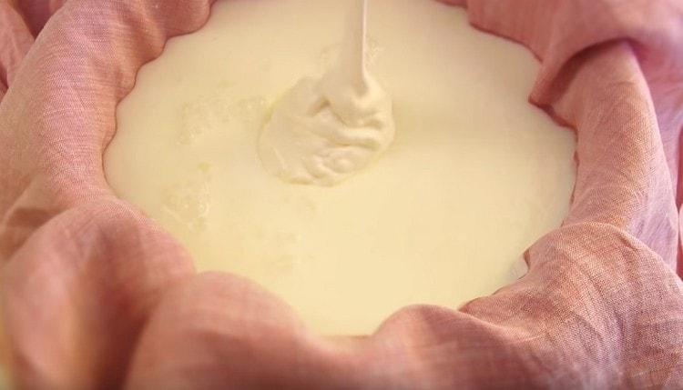 A krémsajt elkészítéséhez öntsünk tejfölt és kefirot egy természetes kendővel borított szűrőedénybe.