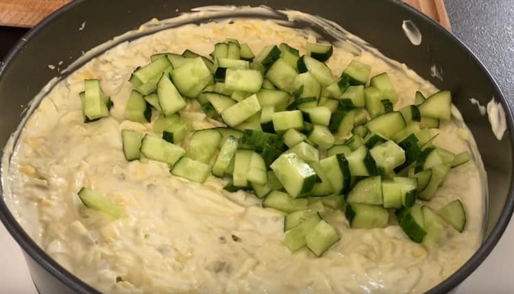 Taglia un cetriolo fresco e forma il successivo strato di insalata.