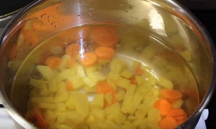 Налейте вода в тиган и добавете към нея картофи и моркови.