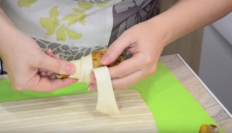 Avvolgi delicatamente ogni coscia di pollo con una striscia di pasta.
