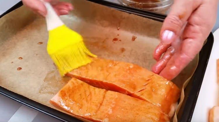 Copriamo la teglia con la pergamena, la ungiamo con la marinata e disponiamo i pezzi di salmone, ungendoli anche con abbondante marinata.