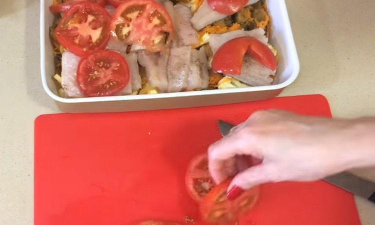 Į kepimo indą dedame daržoves, žuvį, uždengiame pomidoro riekelėmis.