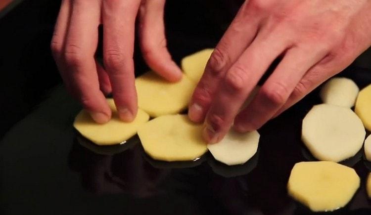Намазвайки лист за печене с растително масло, разпределяме слой картофи.