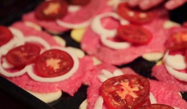 nakrájejte rajče na kruhy a rozložte je na maso na cibuli.