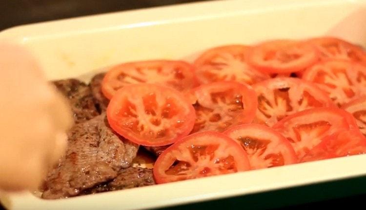 Coprire la carne con pomodori a fette.