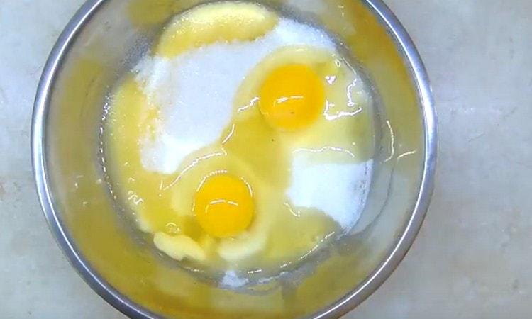 Добавете яйцата и захарта към охладеното масло.
