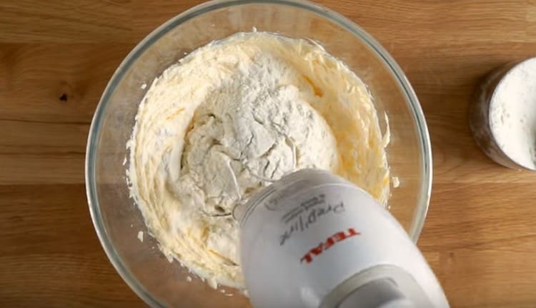 Fügen Sie nach und nach Mehl zum Teig hinzu und schlagen Sie ihn mit einem Mixer auf.