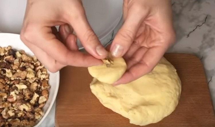 Gumagawa kami ng isang cake sa labas ng isang maliit na piraso ng masa at balutin ang isang piraso ng walnut sa loob nito.
