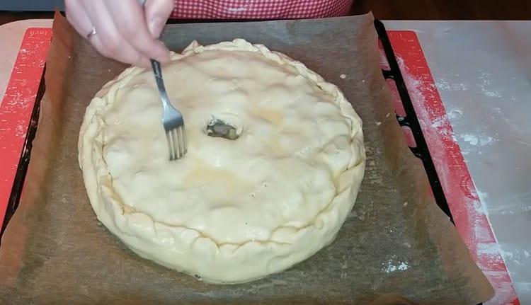 A pite közepén készítsen egy lyukat a gőz kiszivárgására, és több helyen csavarja be a tortát egy villával.