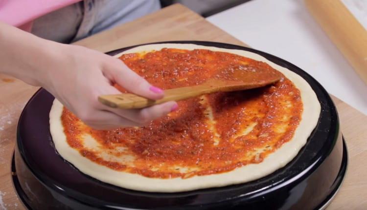 След това намажете основата за пица с доматен сос.