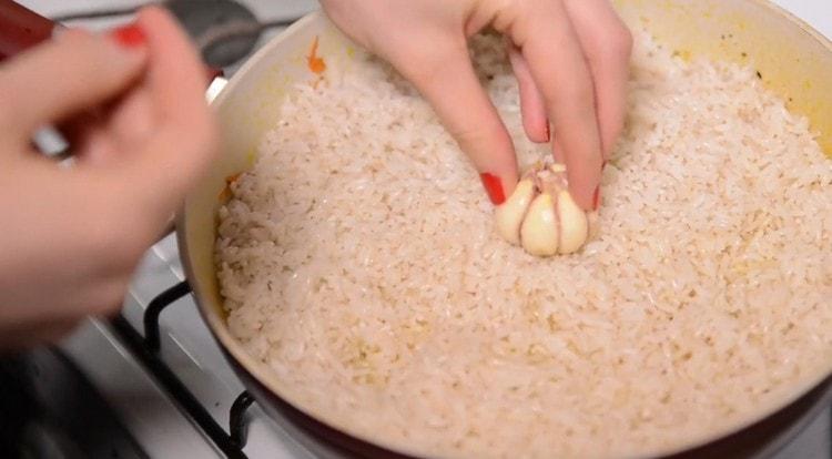 Στο ρύζι στο κέντρο του τηγανιού, κολλάμε ένα κεφάλι σκόρδου.