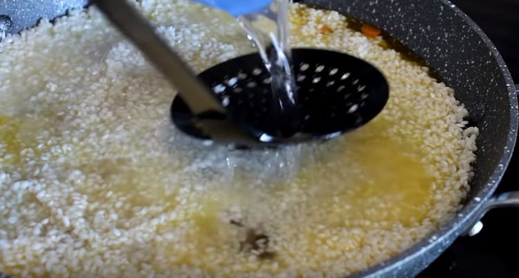 Διανείμετε ομοιόμορφα το ρύζι πάνω από το τηγάνι, γεμίστε το με νερό.