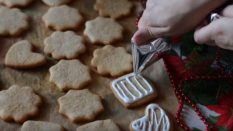 Usando una cornetta o un sacchetto per pasticceria, decorare i biscotti con la glassa.