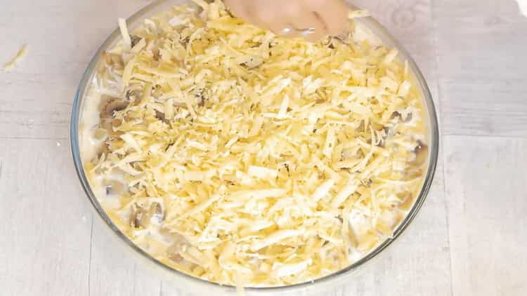 Reiben Sie Käse, um einen Kuchen mit Hühnchen und Champignons zuzubereiten