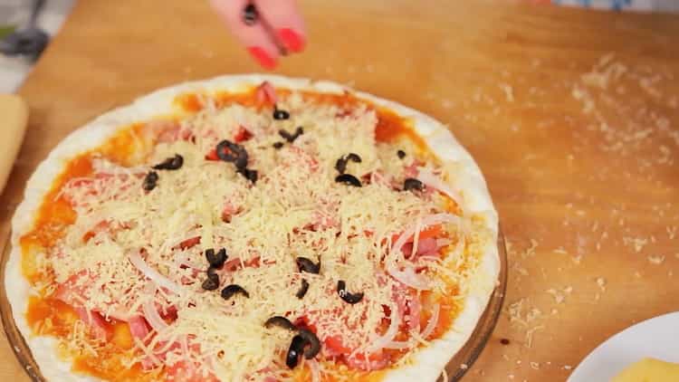 Um Pizza in der Mikrowelle zuzubereiten, geben Sie geriebenen Käse auf den Kuchen
