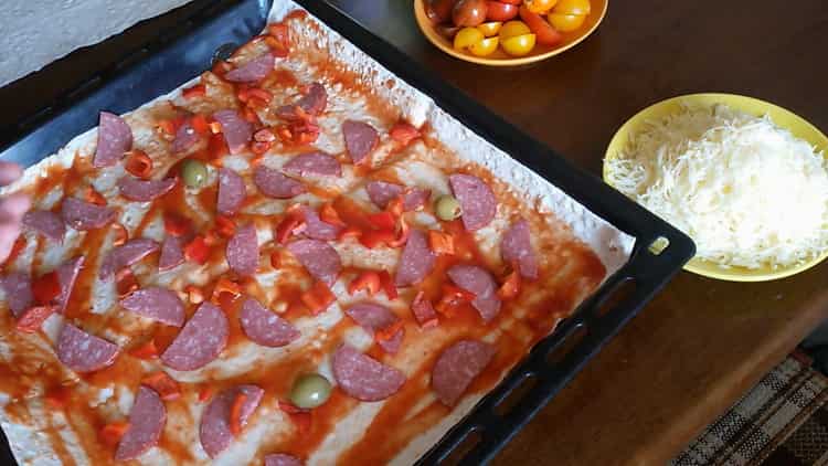 Um Pizza aus Fladenbrot im Ofen zuzubereiten, schneiden Sie die Wurst