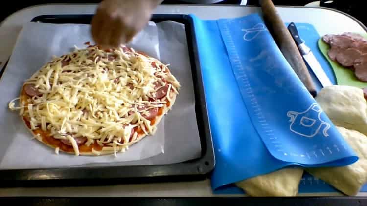 Reiben Sie Käse, um Kefirpizza im Ofen zuzubereiten