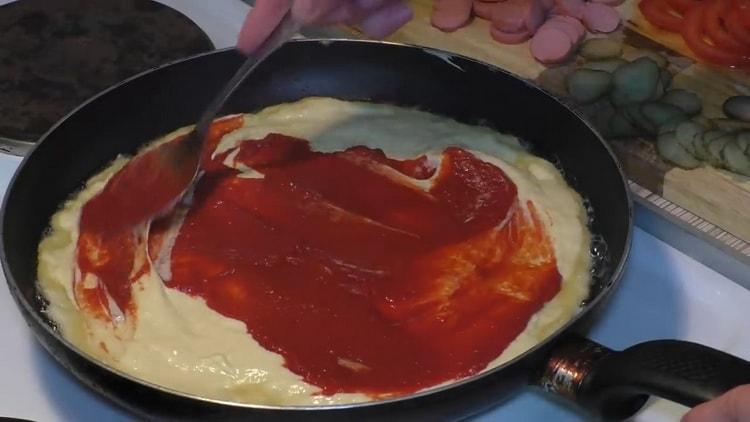 Um Pizza in einer Pfanne zuzubereiten, den Teig mit Sauce einfetten