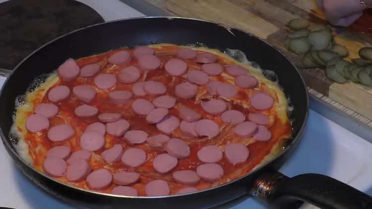 Um eine Pizza in einer Pfanne zuzubereiten, geben Sie eine Wurst auf die Sauce