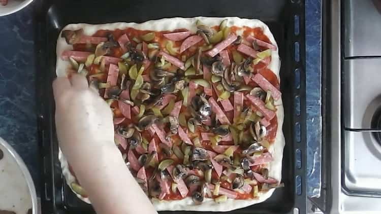 Um eine Pizza mit Gurken zuzubereiten, geben Sie die Pilze auf den Teig