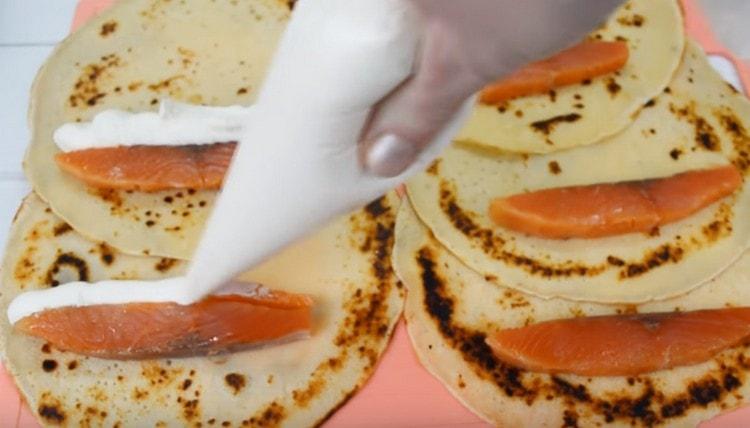 Distribuiamo un pezzo di salmone su ogni pancake e spremiamo il formaggio cremoso vicino ad esso.