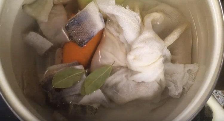 Wir füllen den Knoten mit den Resten von Fisch, den Scheiben selbst sowie Zwiebeln, Erbsen, Erbsen, Karotten und Lorbeerblättern mit Wasser in einem Topf.